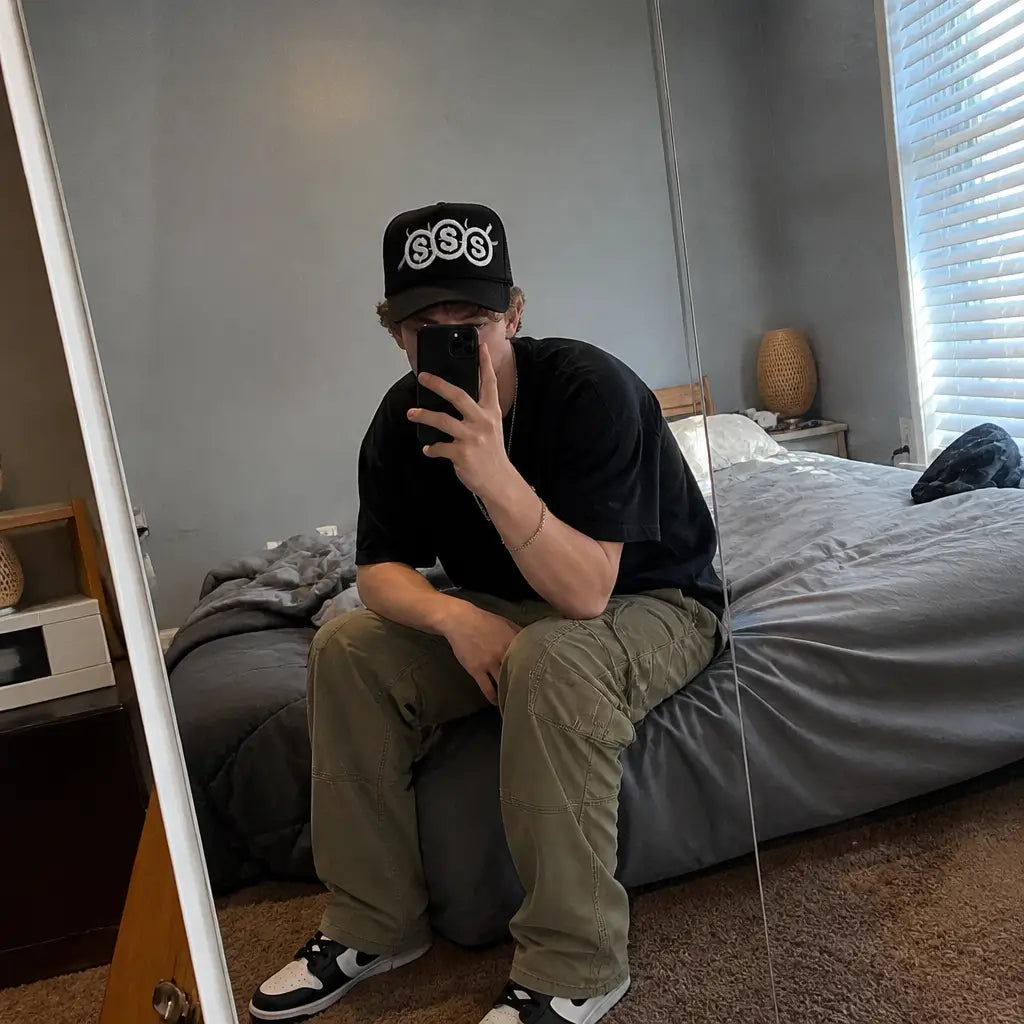 Bedroom mirror selfie wearing the SSS trucker hat with an oversized tee and cargo pants